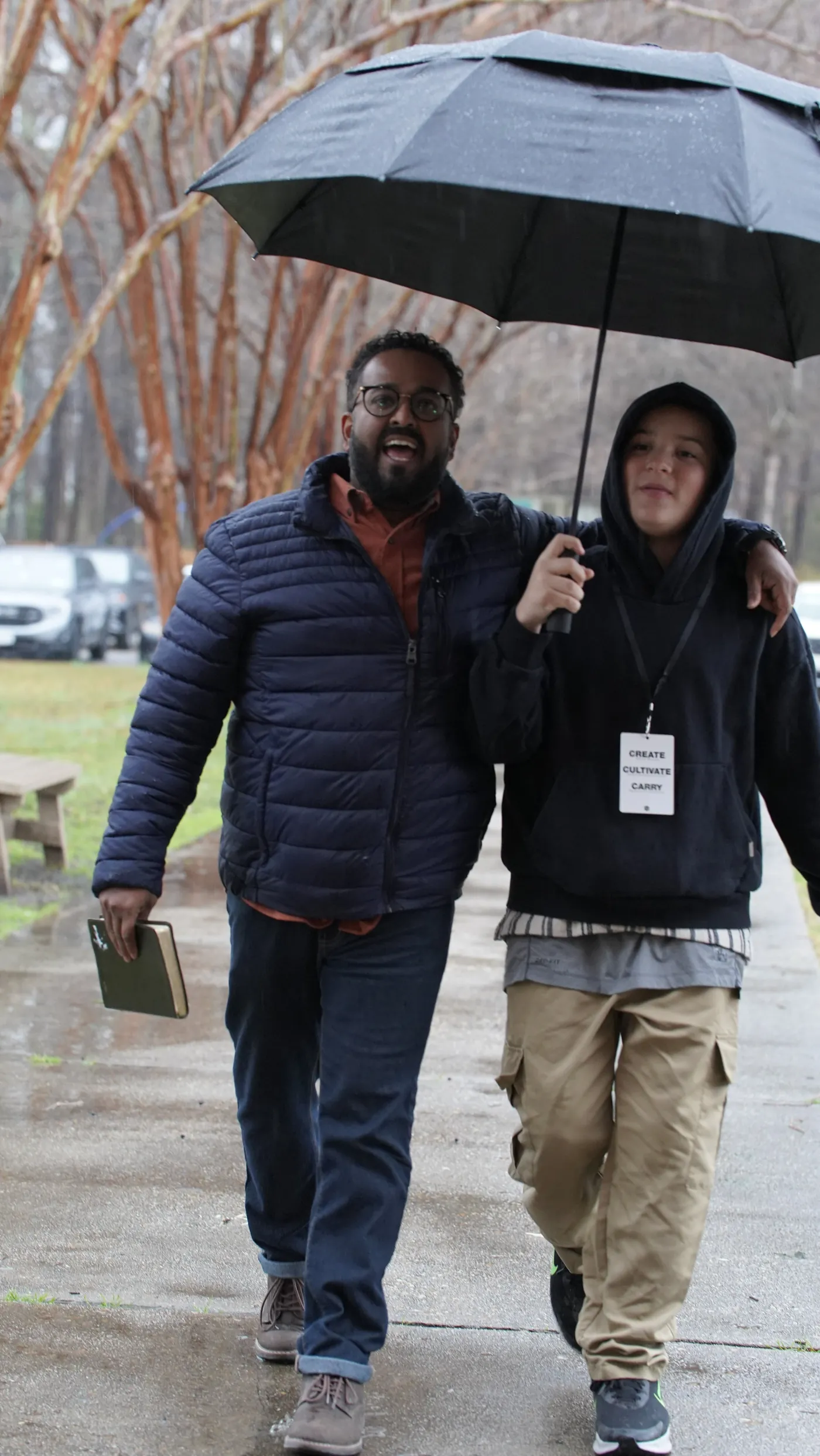 A man walking a younger man under one umbrella, Bible in hand
